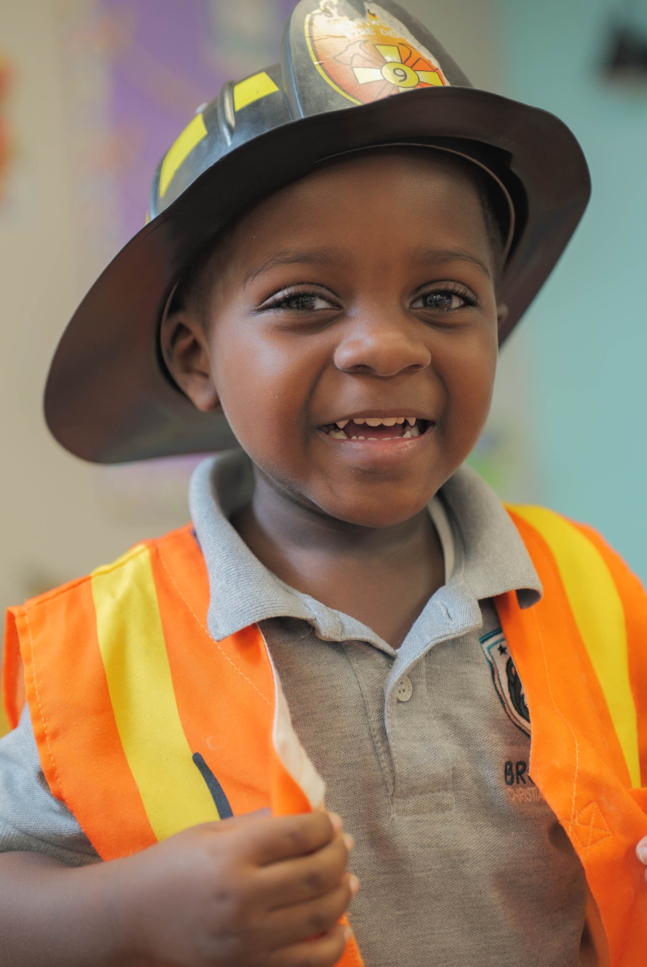 Smiling preschool boy wearing a firefighter hat and safety vest during dress-up play